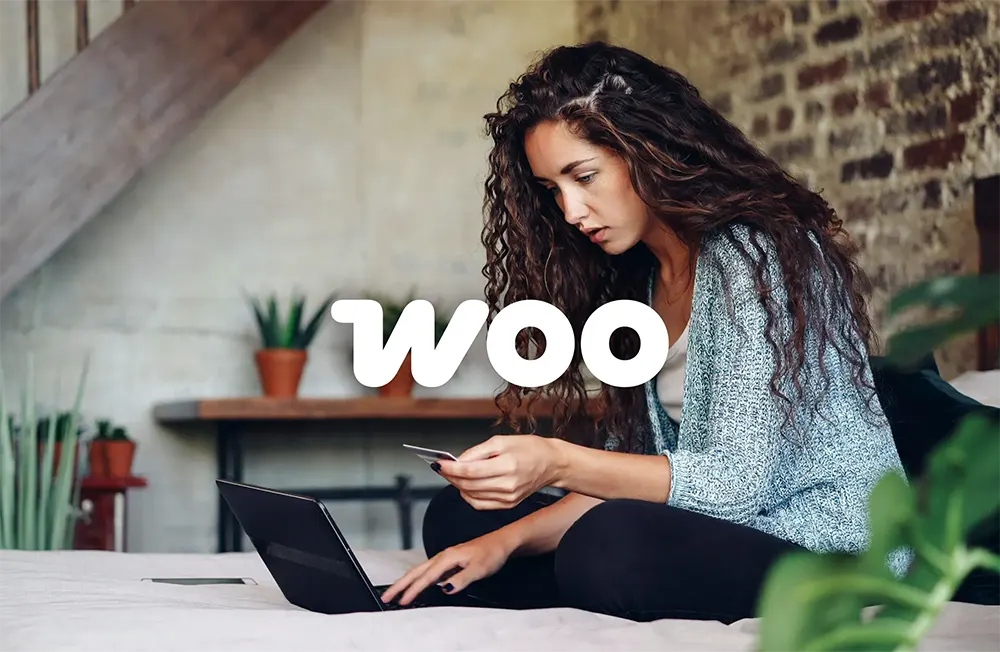 Person entering their credit card information on a website and a WooCommerce logo overlaying.